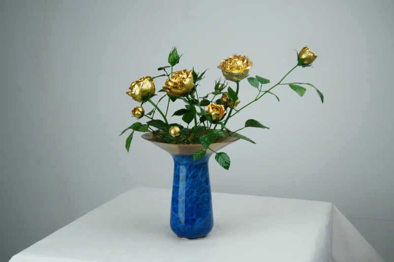 蓝色纹理花瓶中插有金色花朵与绿色枝叶的铜艺作品